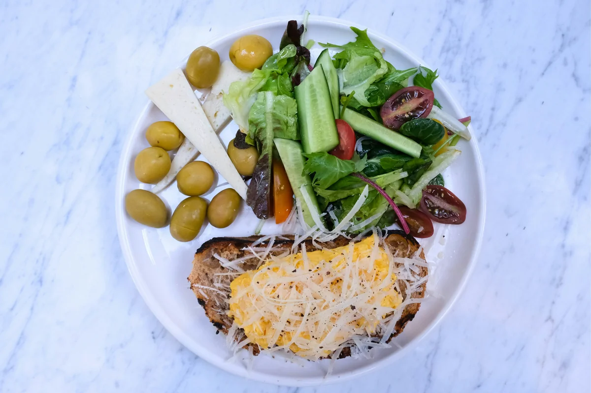A vibrant Mediterranean breakfast featuring olives, cheese, and seasonal greens on a white plate. - balanced meals