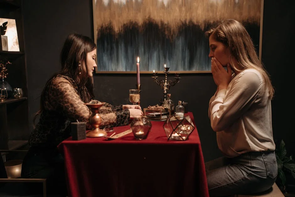 Two women engrossed in a mystical fortune telling session with candles and tarot cards on a dimly lit table. - live medium readings