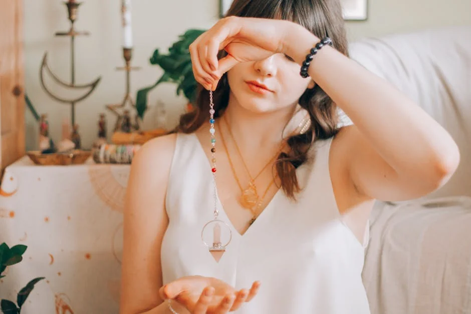 Young female with dark long wavy hair and swinging crystal pendulum over hand while soothsaying future - spiritual awakening signs