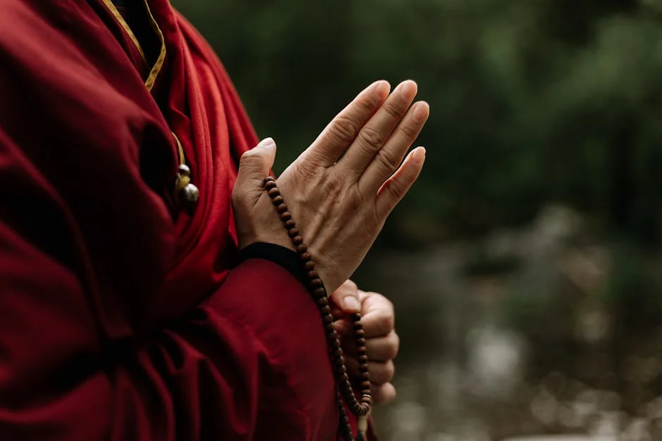 Close-up of monk in red robe meditating with prayer beads outdoors. - spiritual awakening signs