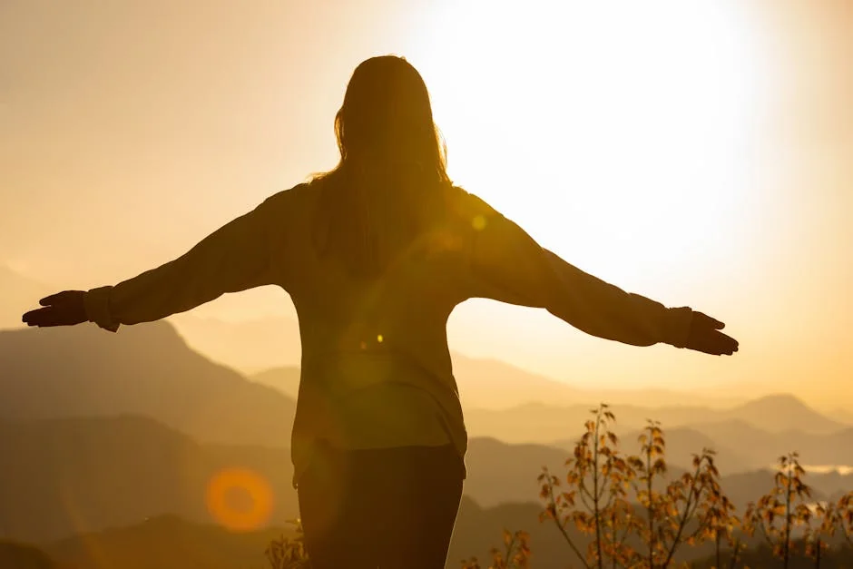 A woman stands with arms open, embracing the sunrise in a mountainous landscape, creating a tranquil silhouette. - spiritual awakening signs