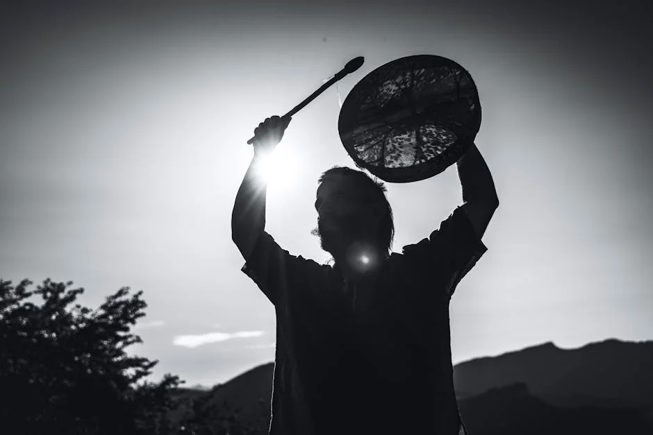 A dramatic black-and-white silhouette of a shaman holding a drum against the mountainous backdrop of Lombardia, Italy. - spiritual awakening signs