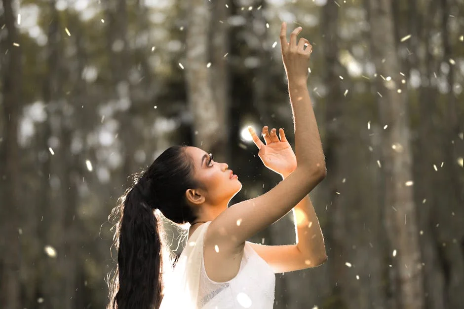 A woman in white gracefully reaches towards floating particles in a serene forest setting. - spiritual awakening signs